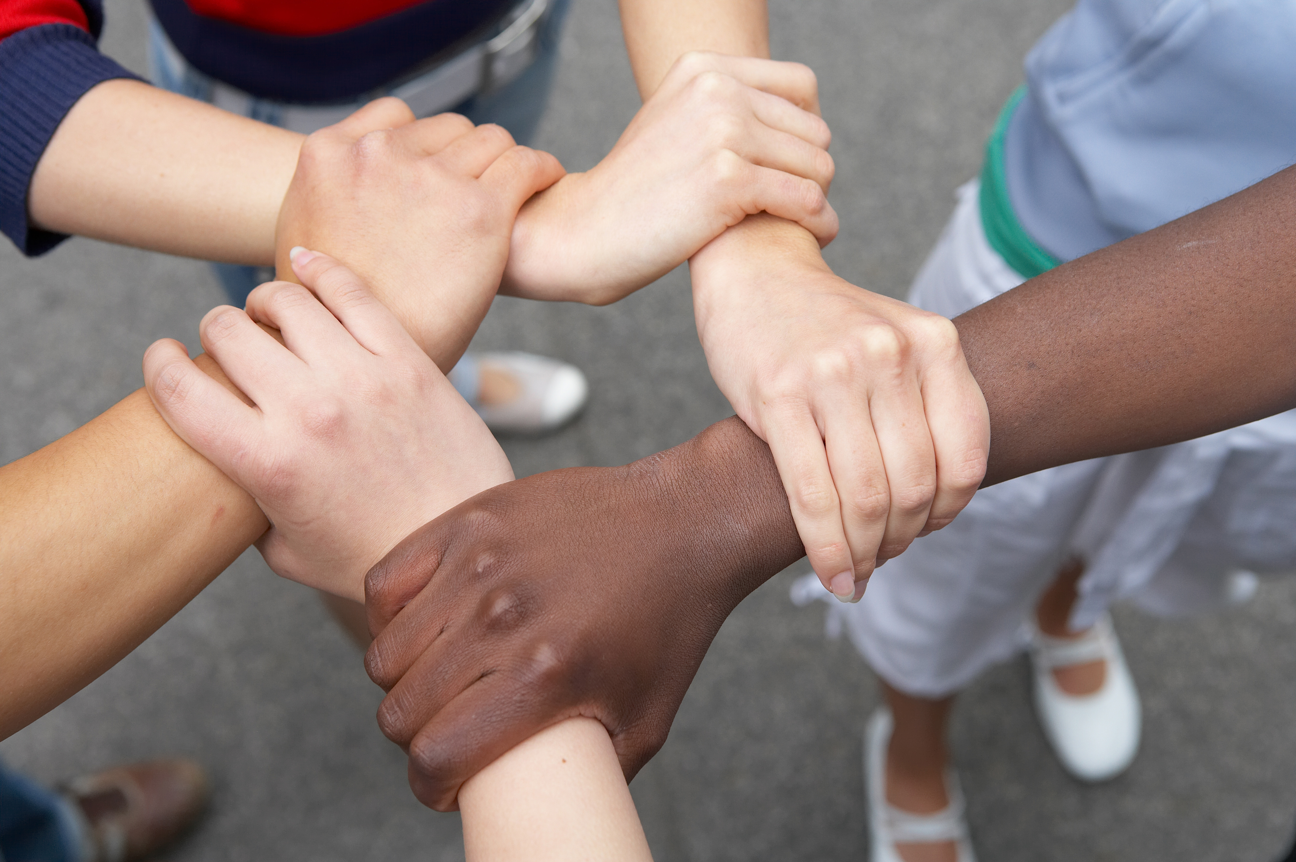 Personen  verschiedener Hautfarben stehen auf Straße und greifen an Handgelenk, sodass ein Kreis entsteht (Ansicht von oben)reis